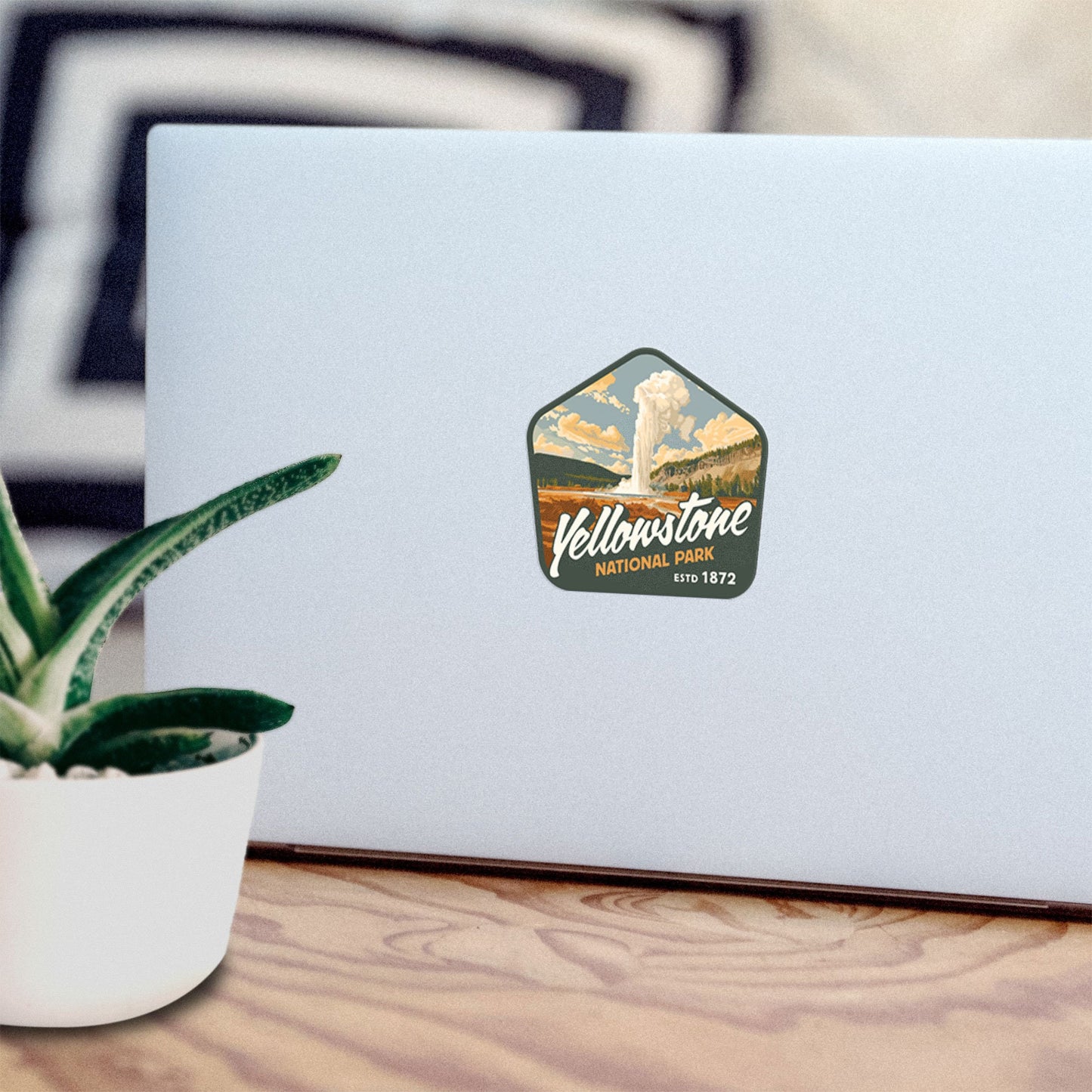 Waterproof vinyl sticker of Yellowstone National Park adorning a laptop, with a plant in the foreground. Perfect for nature lovers, this hiking sticker features stunning mountain art and is ideal for laptops, water bottles, and more.